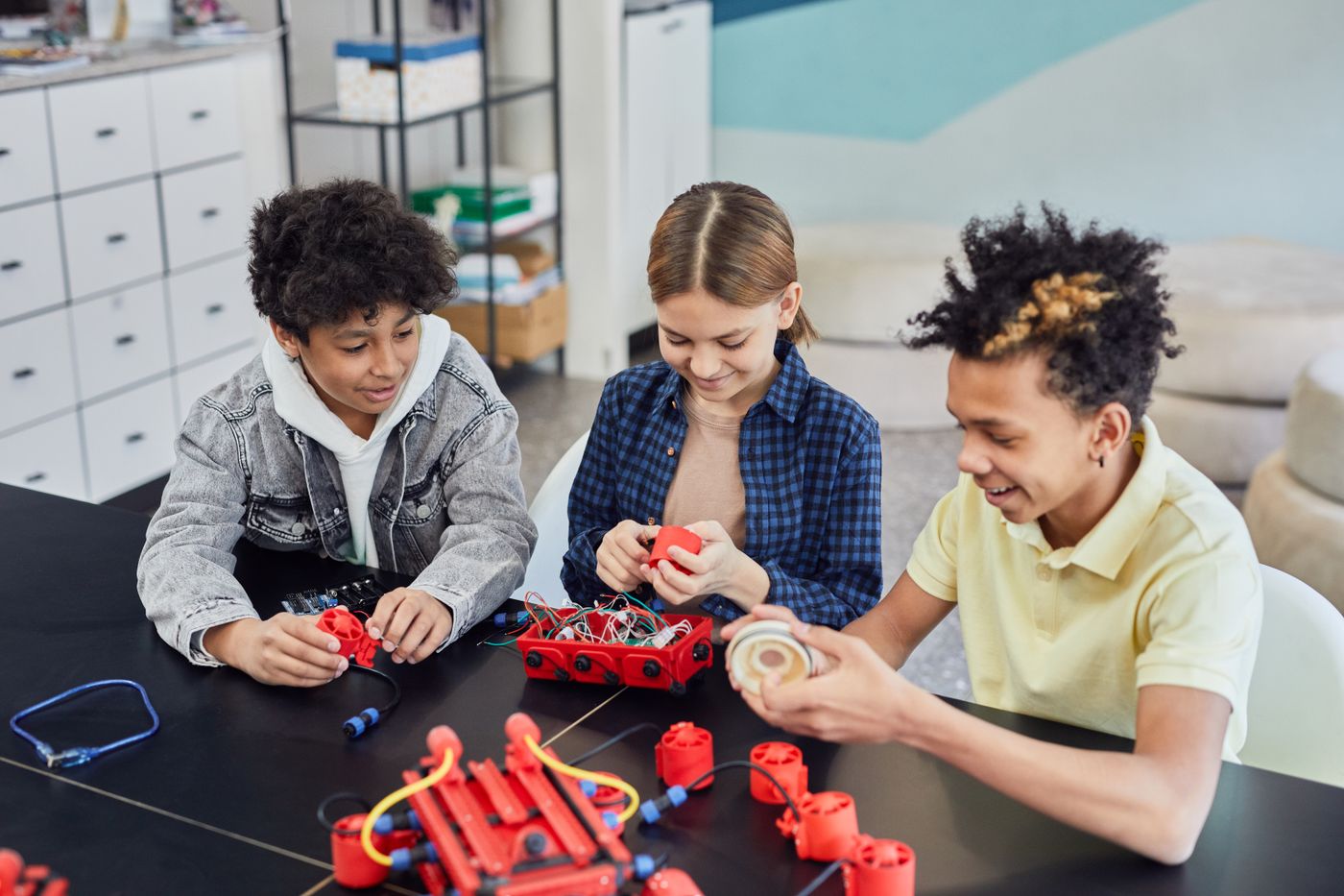 Three students collaborate on a robotics build at a shared table