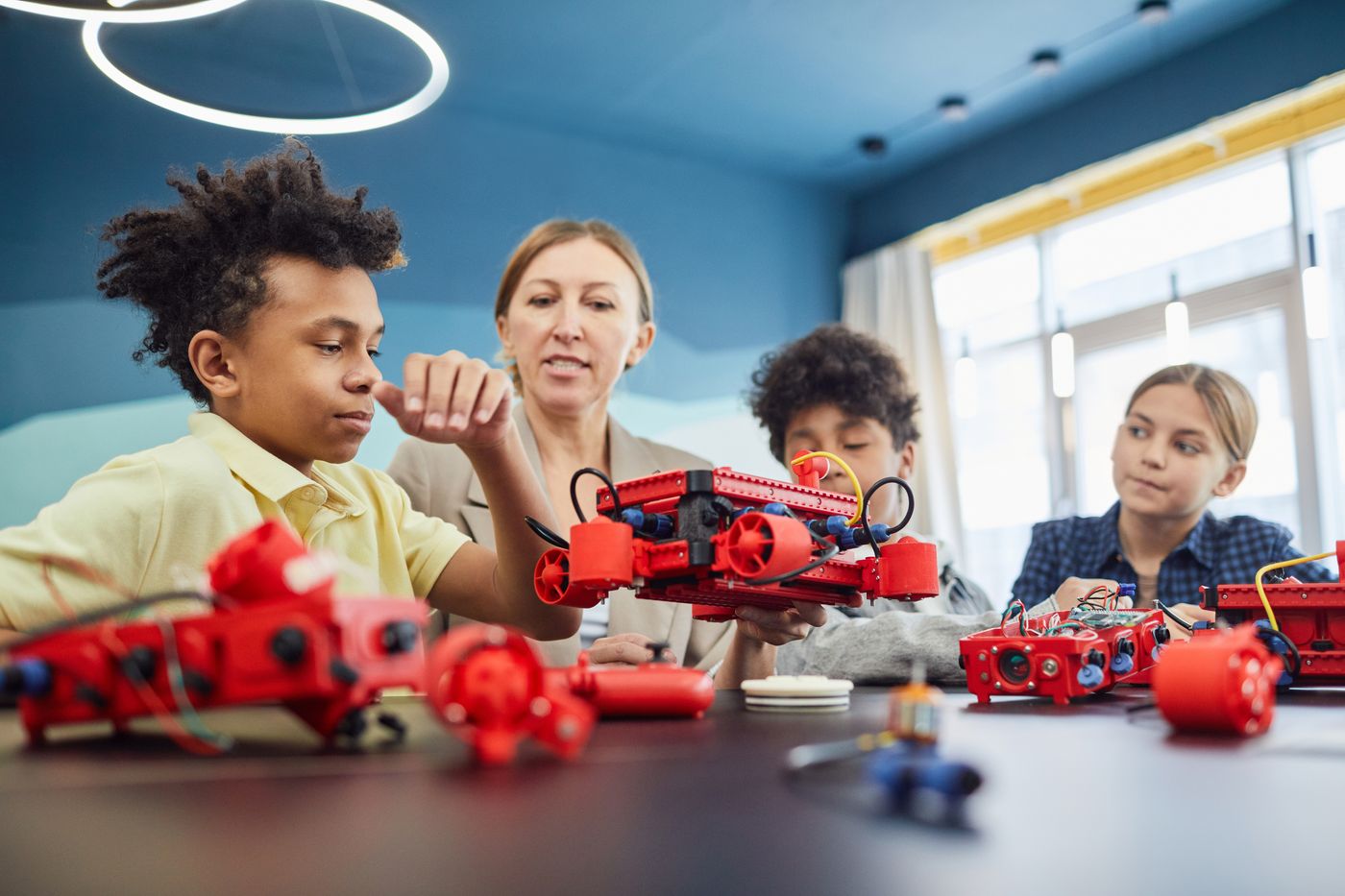 A teacher works alongside students as they build robots in a bright classroom